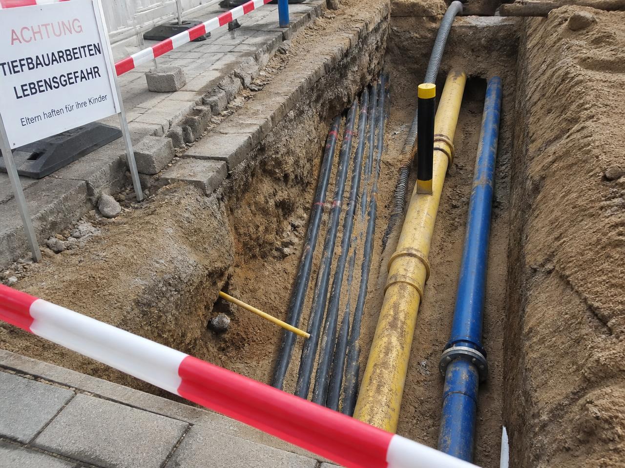 Blick in einen offenen Graben mit freigelegten Kabeln, einer Gasleitung und einer Wasserleitung